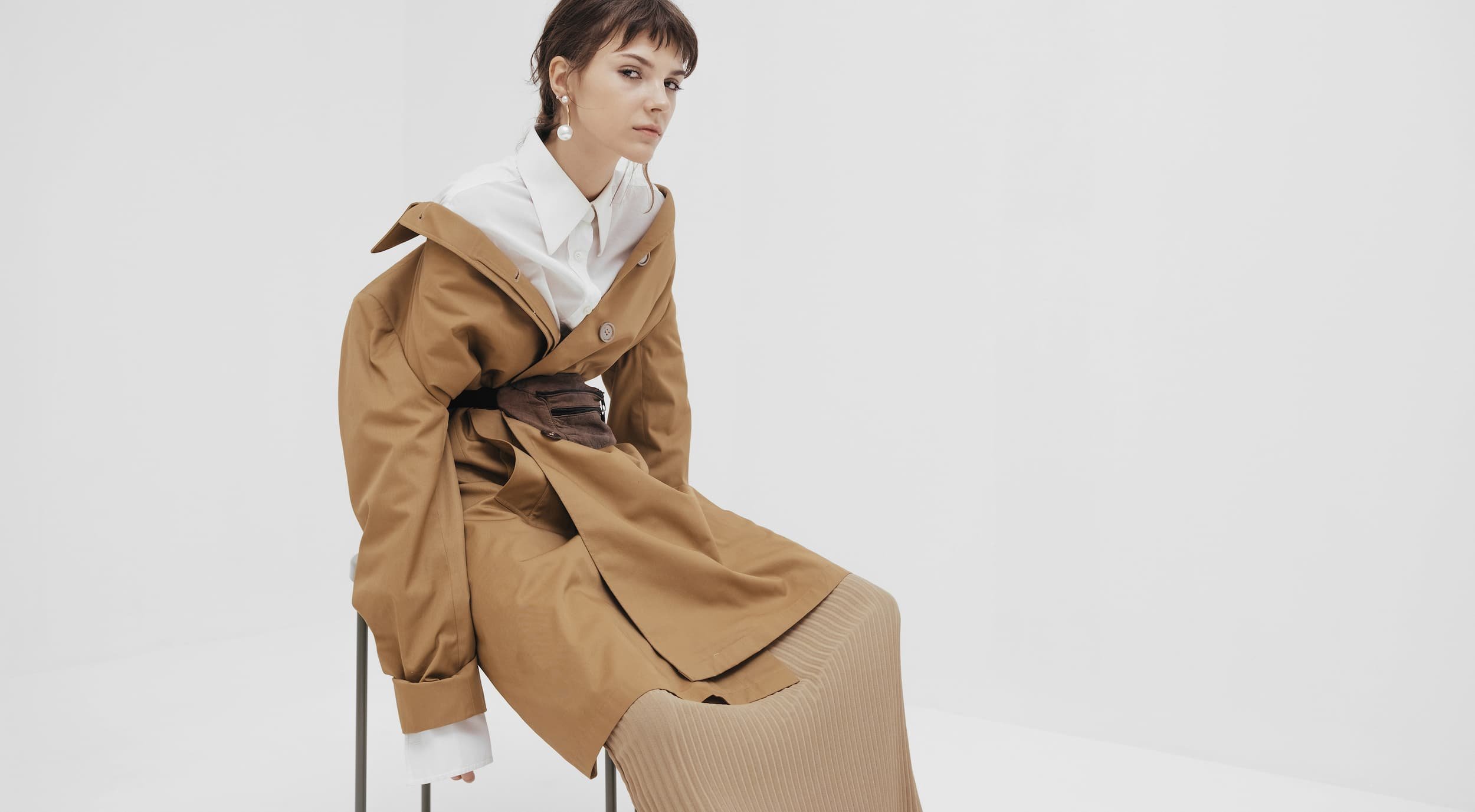 woman slouching on a stool in a long belted khaki jacket
