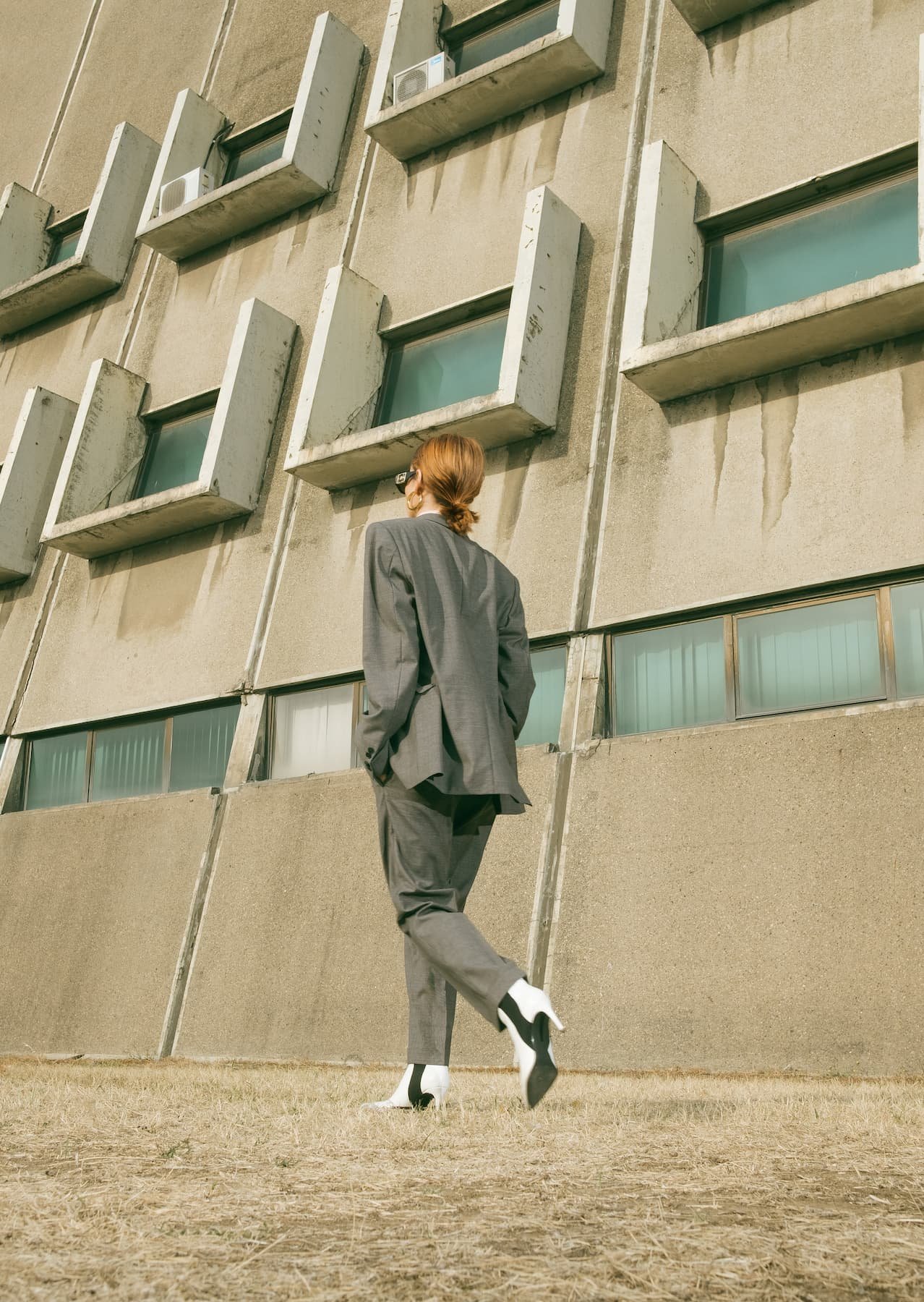 woman in a grey suit walking away in front of a concrete building