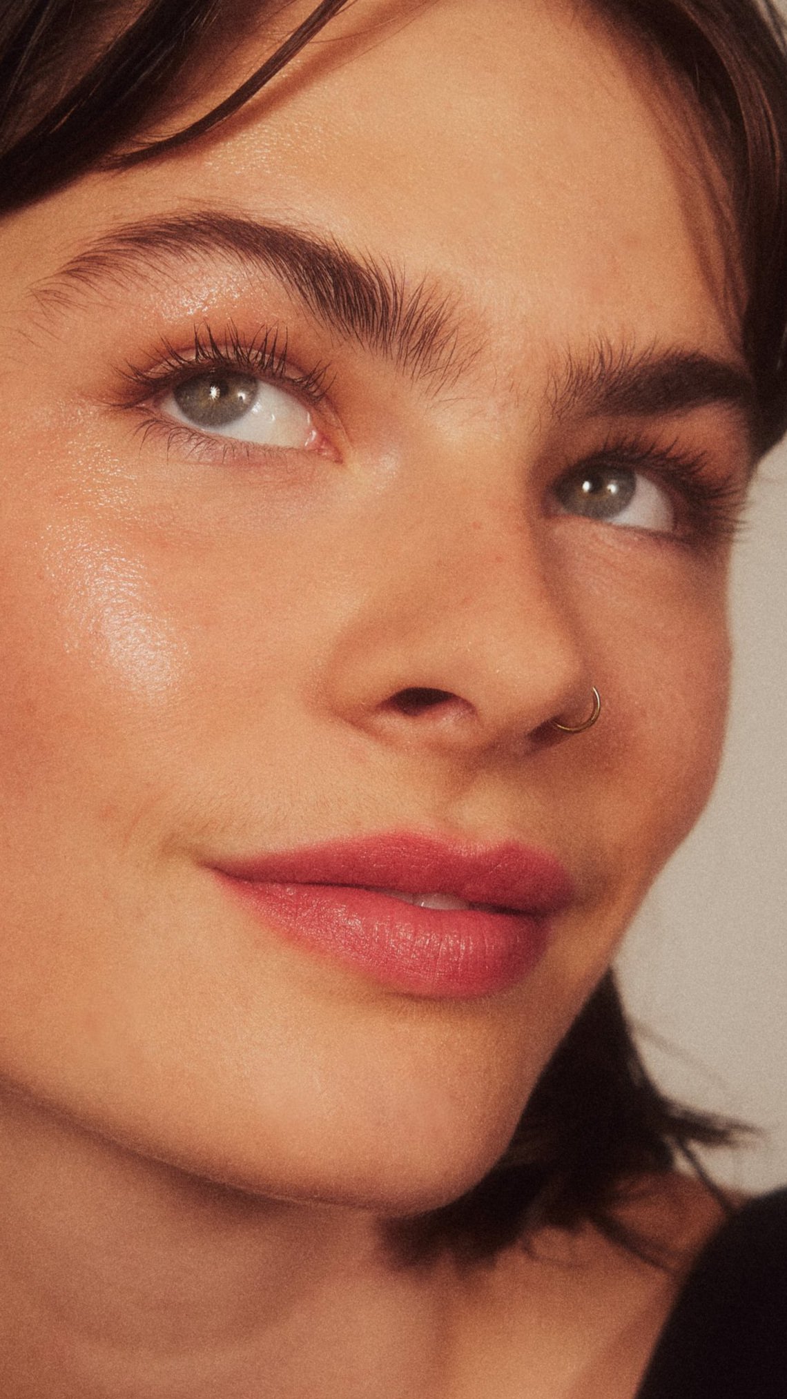 Nahaufnahme eines Gesichts mit blauer Augen, dunkelbraunen Haaren, Lippen mit rotem Lippenstift, Sommersprossen und einem Nasenpiercing.