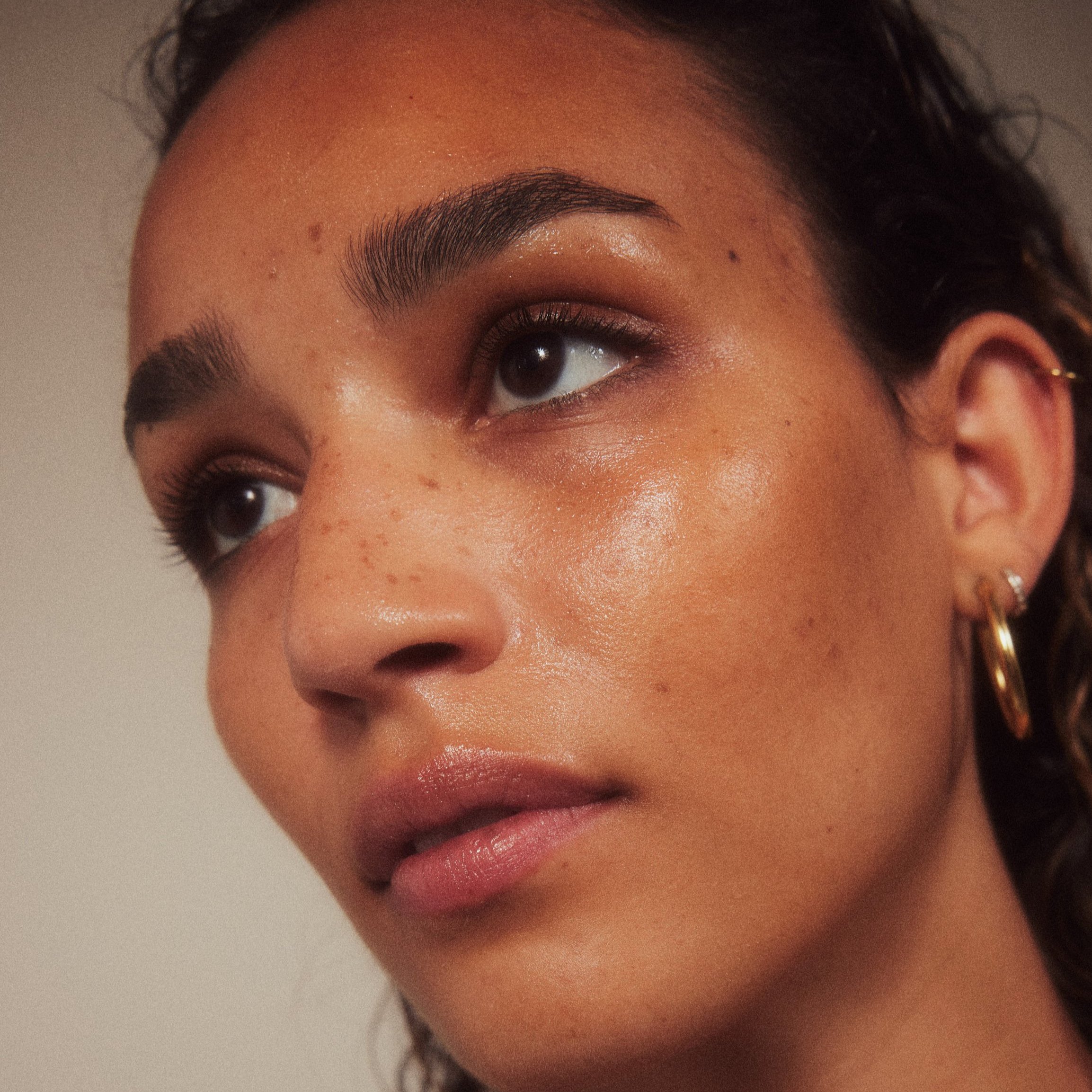 Nahaufnahme eines jungen Frauengesichts mit glatter Haut, dunklen Augen, dichten Augenbrauen, getragenen Ohrringen und natürlichem Make-up.